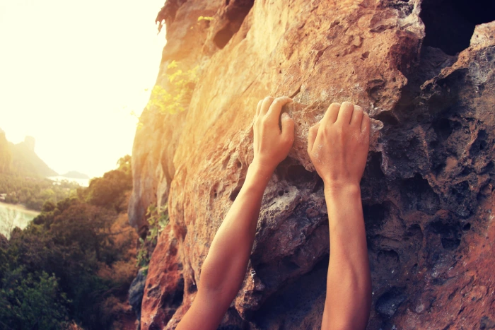 a close up of two arms of a person climbing a rocky cliff